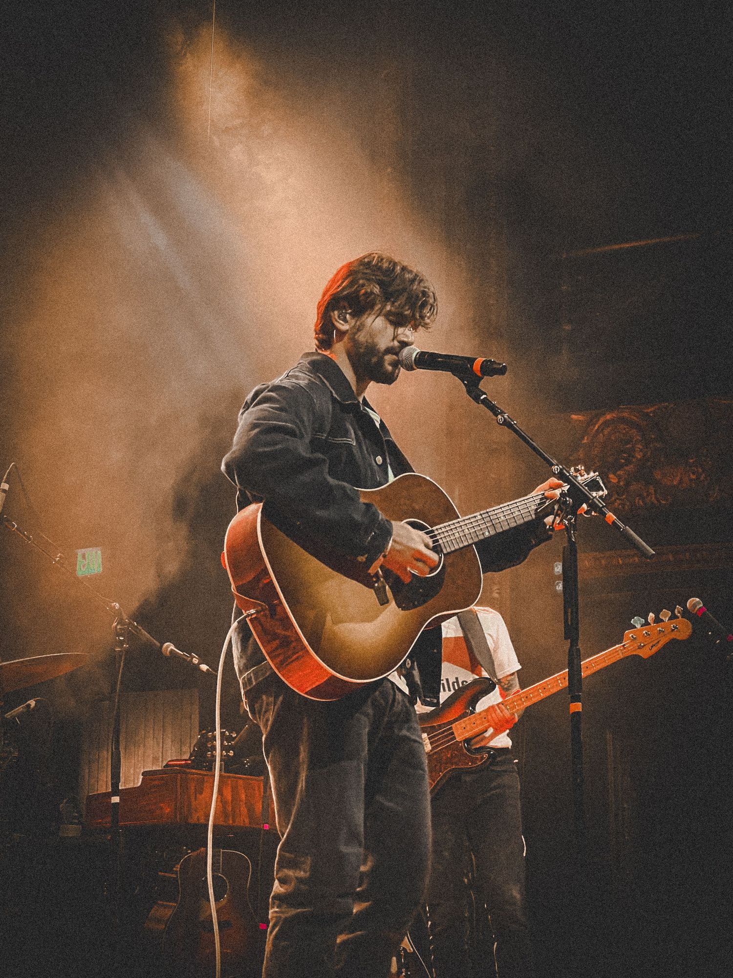 A musician performs on stage with an acoustic guitar under dramatic orange lighting during a live concert performance.