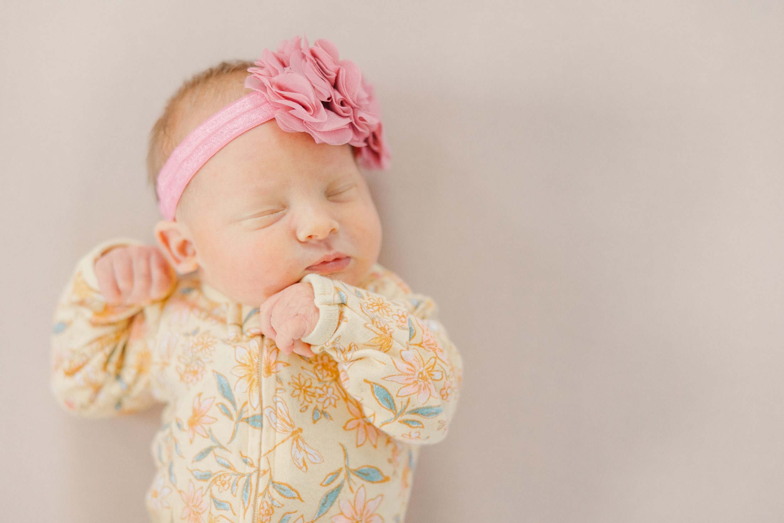 Sleeping newborn baby wearing pink and floral outfit in soft natural light.