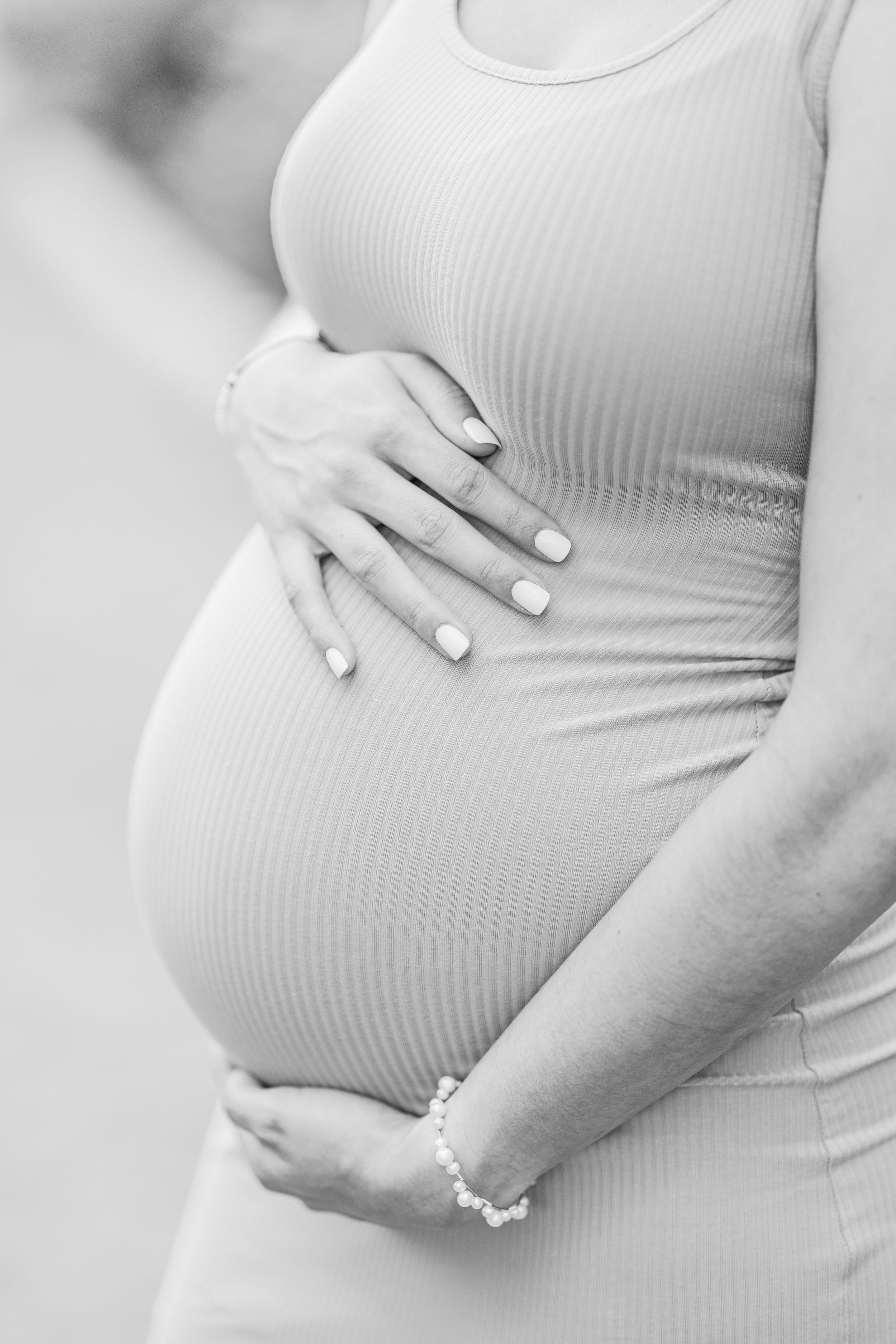 Close-up of hands cradling pregnant belly in ribbed white fabric.