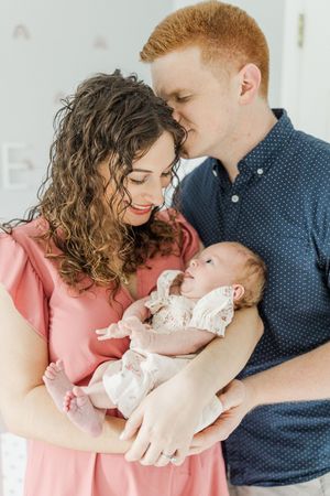 Indoor family portrait session with newborn baby in soft, natural light.