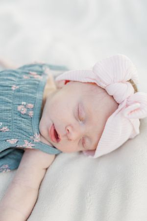 Sleeping newborn baby wearing a pink bow headband and floral dress.