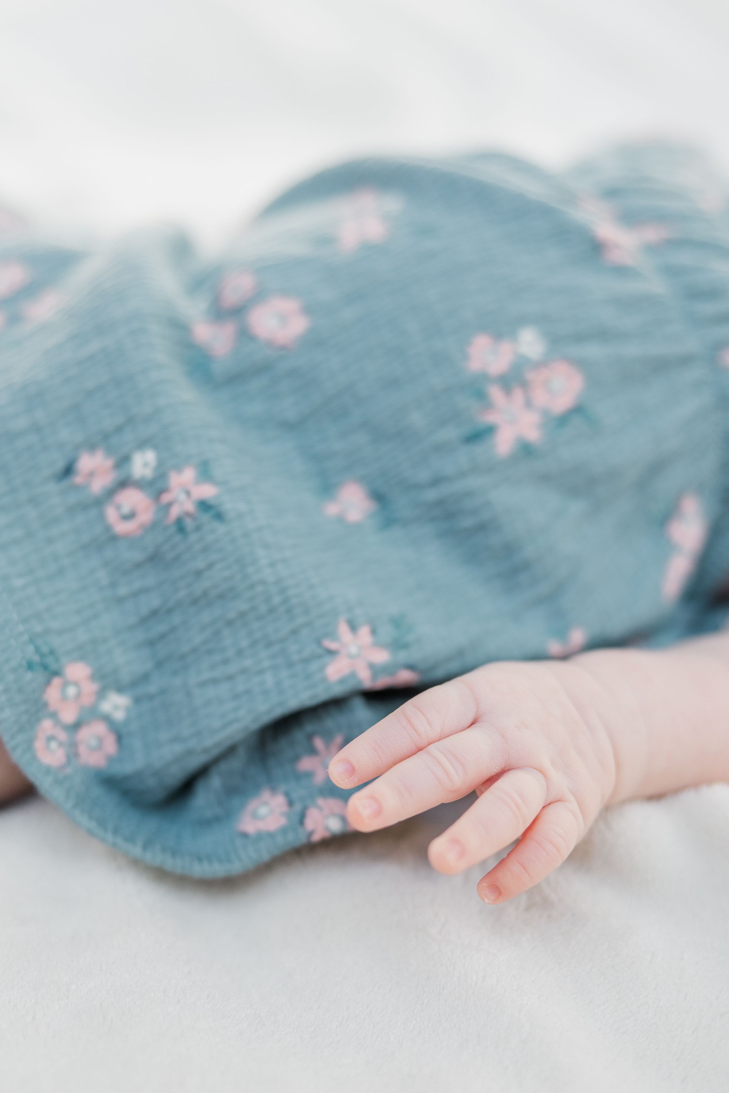 Close-up of tiny baby hand resting on blue floral fabric.