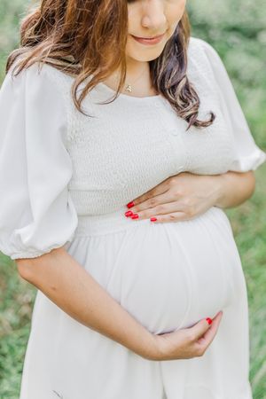 Maternity photos showing woman in white dress touching her pregnant belly.