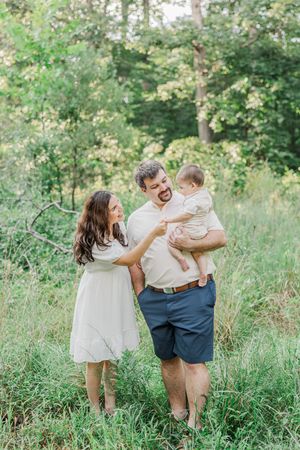 Family playing together in a sunlit meadow with tall grass and trees.