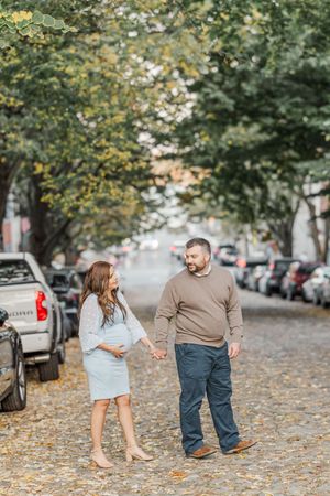 A couple shares a moment on a tree-lined cobblestone street during a maternity photoshoot.