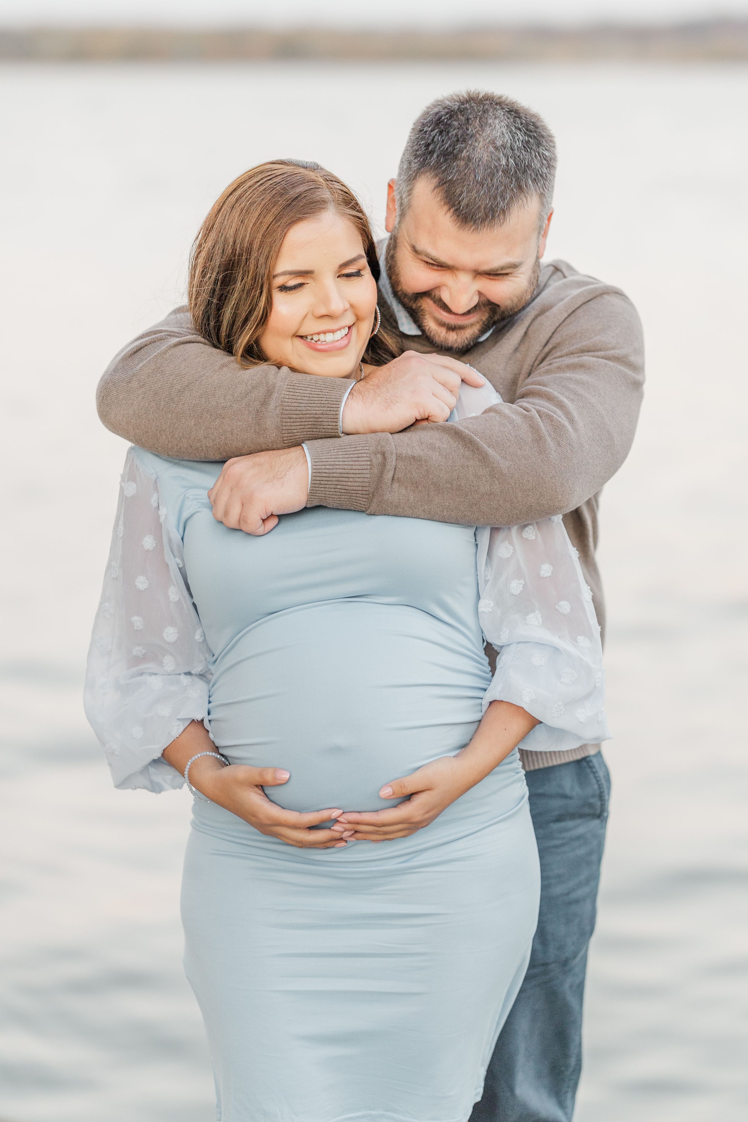 A tender embrace captured during a maternity photo session on a bright day.