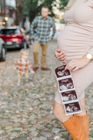 Couple holding ultrasound photos on fallen autumn leaves in an outdoor setting.
