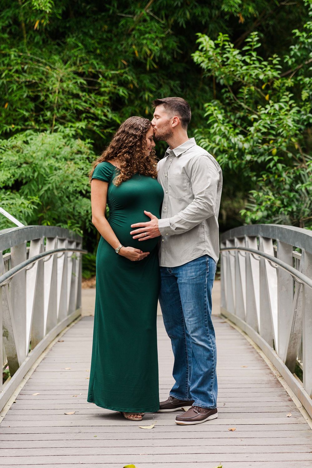 A couple shares a tender moment on a white wooden bridge surrounded by lush green foliage.