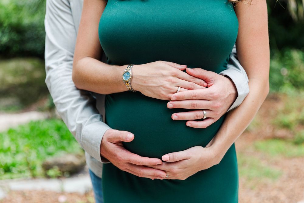A series of photos showing hands gently cradling a pregnant belly in a dark green maternity dress against a natural backdrop.
