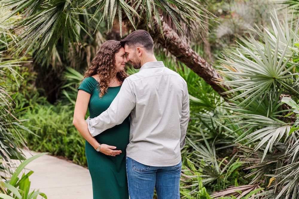 A couple in casual attire embraces while walking through a lush tropical garden setting.