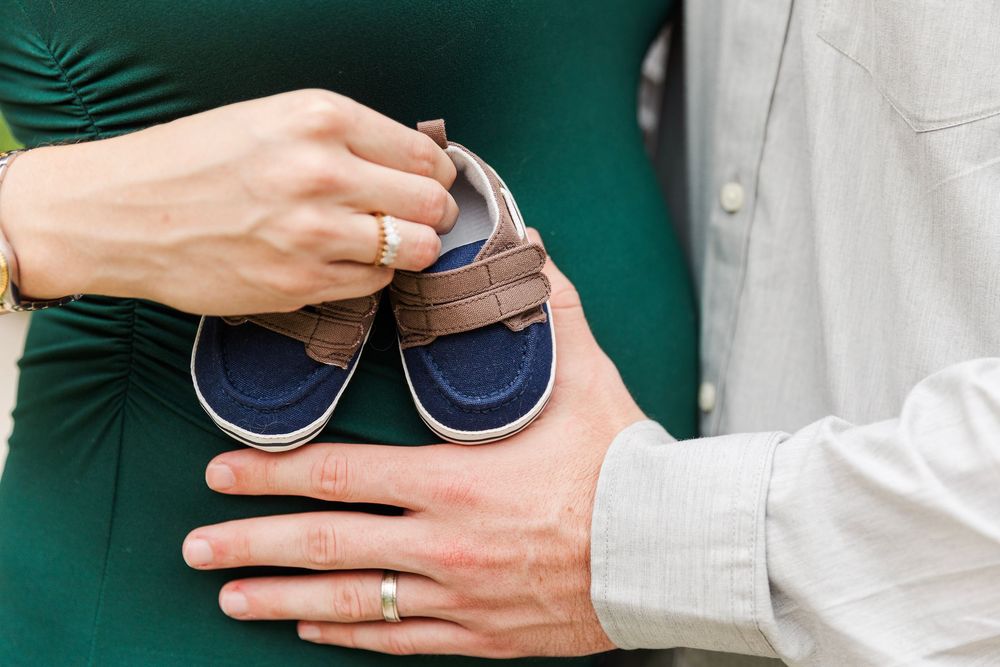 Hands exchanging a small blue baby shoe in a nursery setting with green and white background.