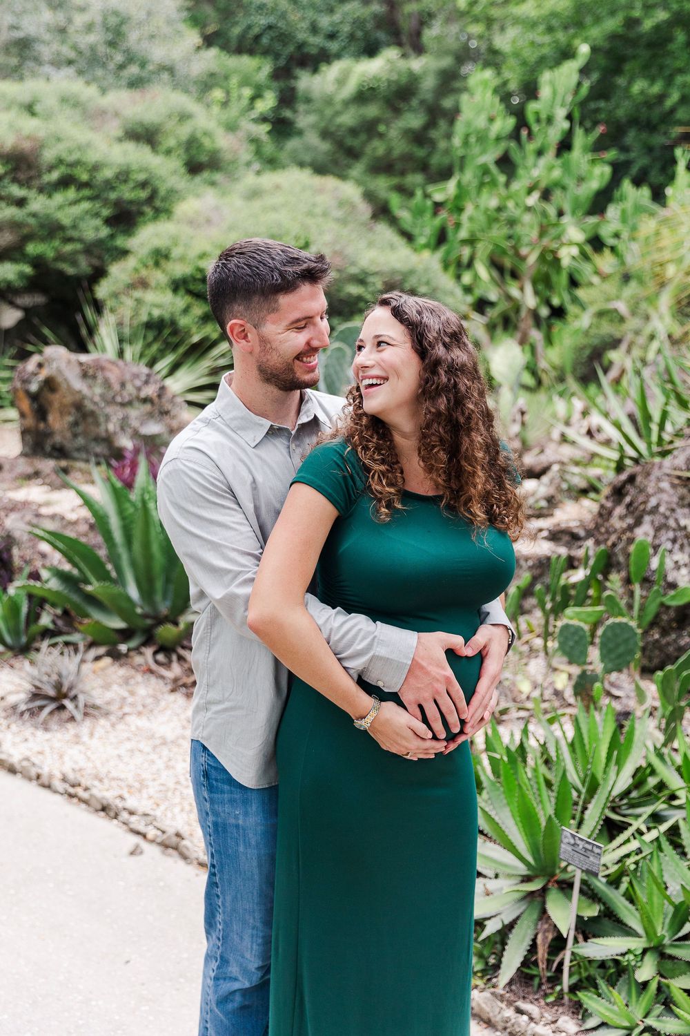 A couple shares romantic moments in a lush garden setting while wearing green and gray outfits.