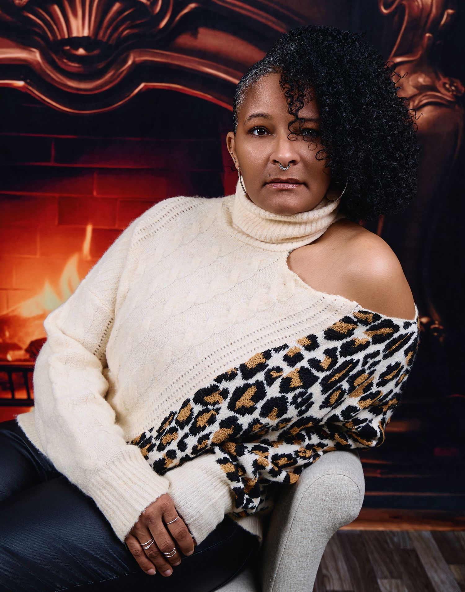 Fashion portrait in cream leopard print sweater by warm fireplace.