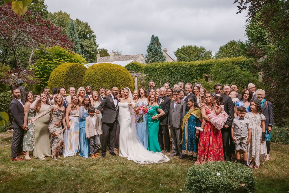 Large group of wedding guests gathered outdoors in a garden setting for formal photos.