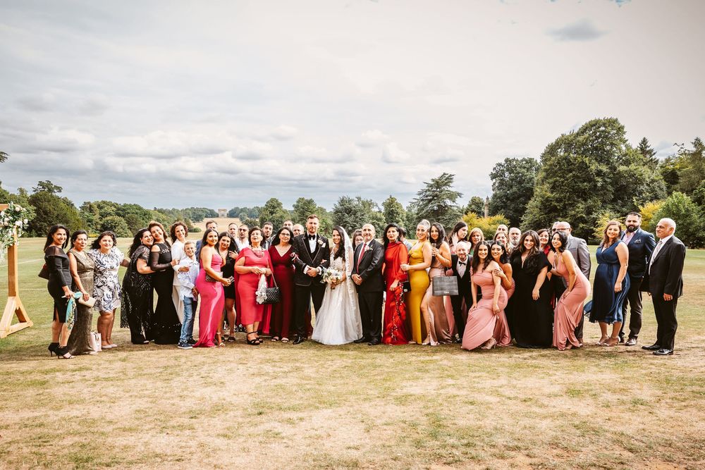 Large wedding party gathered outdoors in a scenic field during a sunny afternoon celebration.