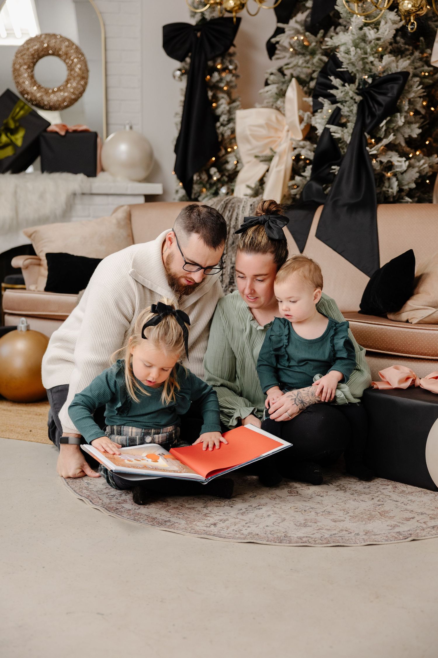 A family reads books together while lying on a carpeted floor during a cozy holiday moment.