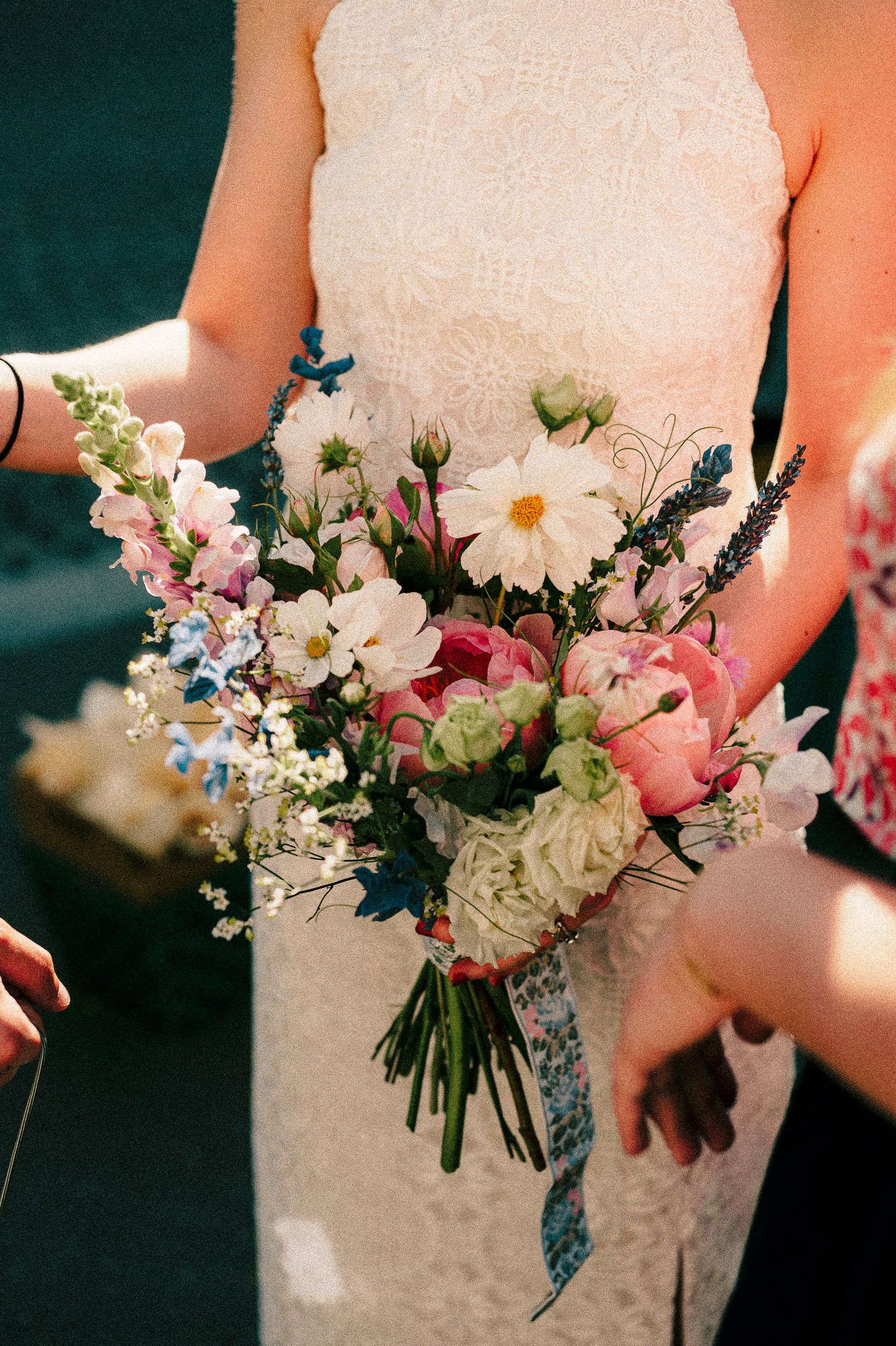 A row of elegant wedding bouquets featuring white daisies, roses and delicate blue accents held against a dark background.