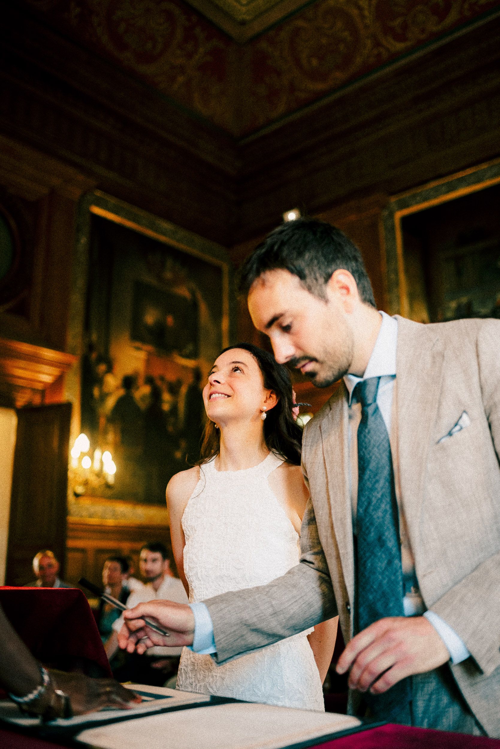 A couple shares an intimate moment while signing their marriage certificate in an elegant, ornate room.