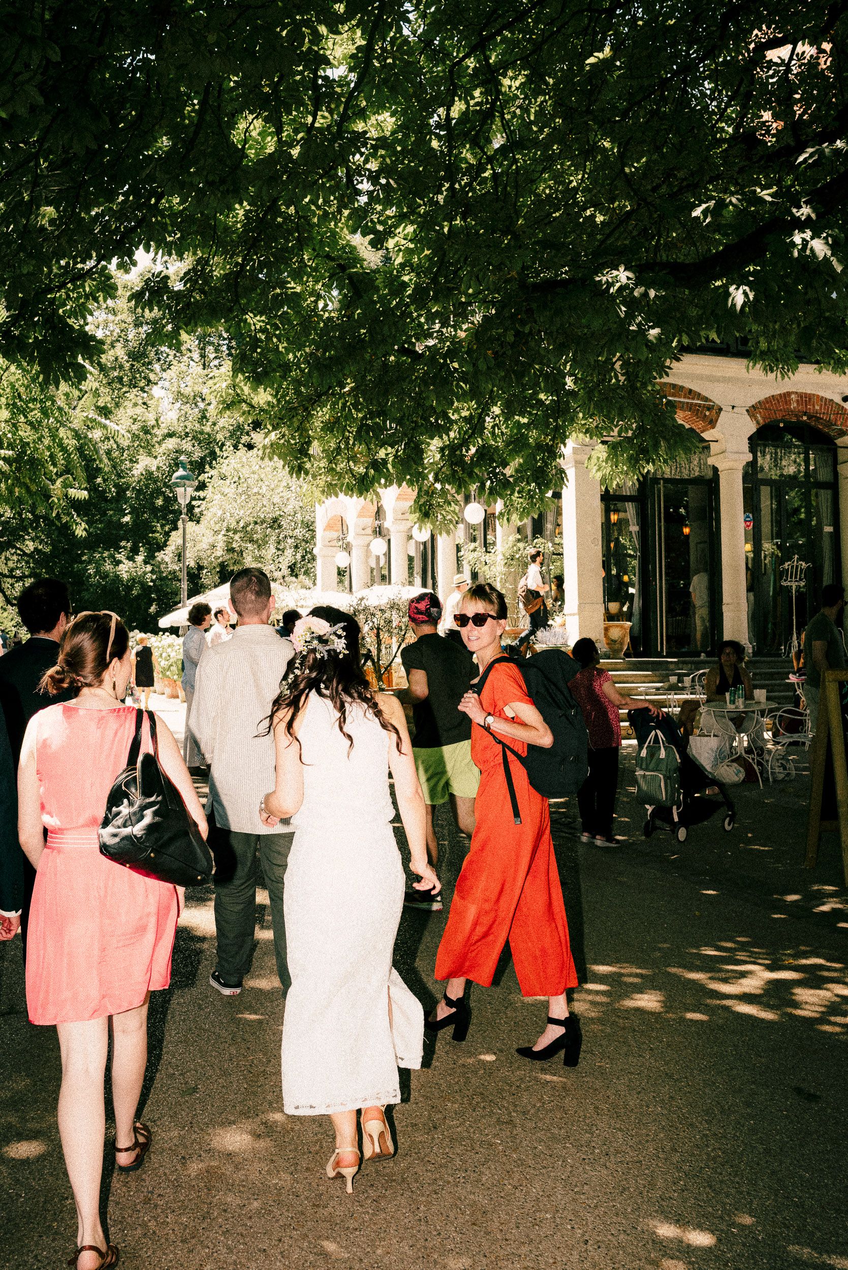Wedding party mingles on a tree-lined path during a summer outdoor reception.