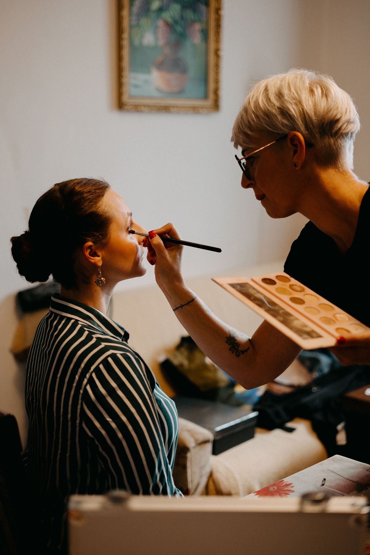 Wedding preparation scene showing makeup application in a softly lit room.