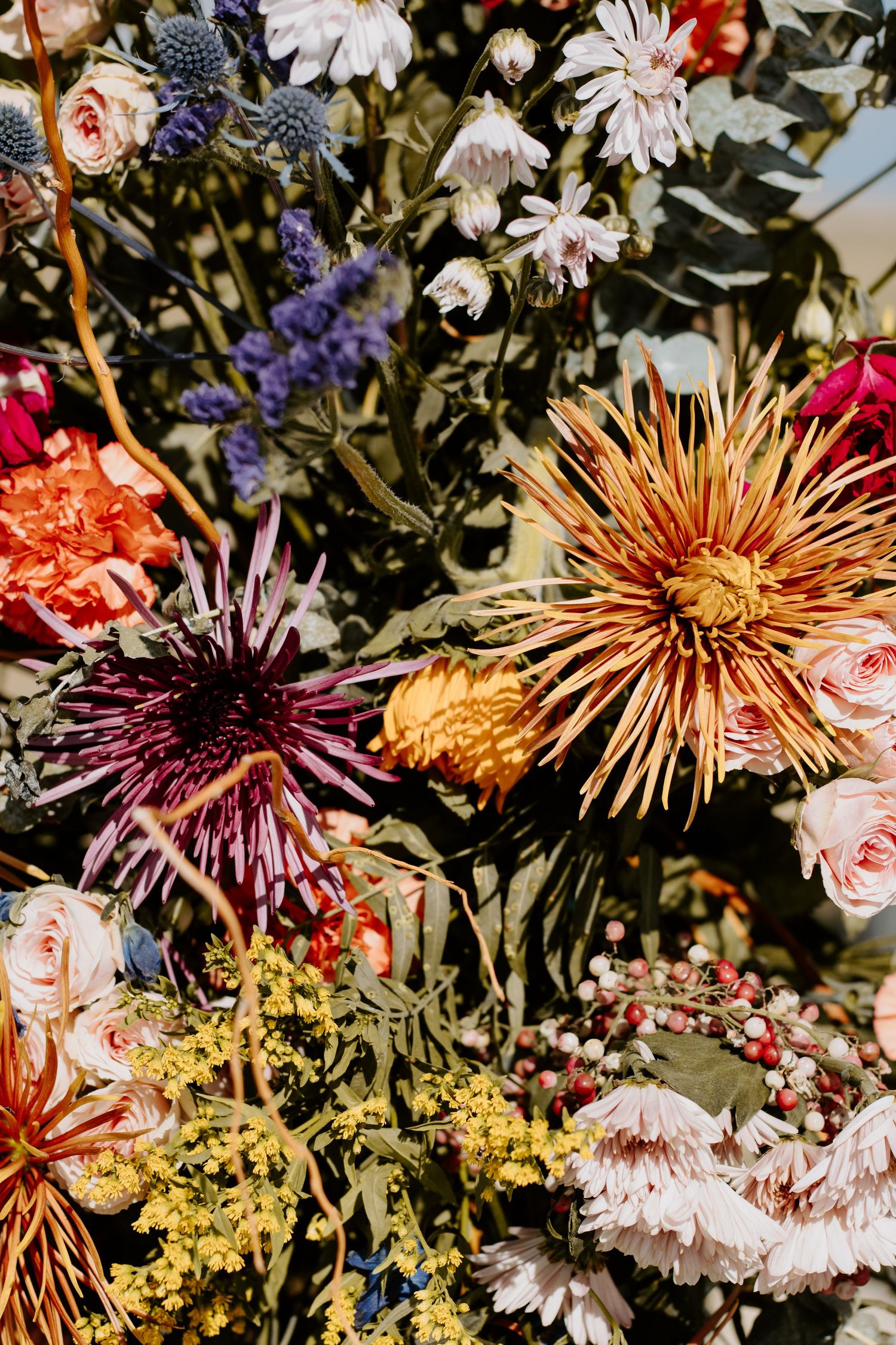 Vibrant mixed floral arrangement featuring dahlias, roses, lavender, and wildflowers in warm autumn tones.