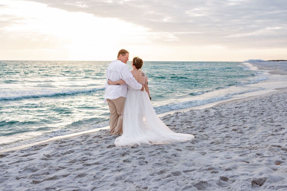 A couple in wedding attire shares a romantic moment walking along a pristine white sand beach at sunset.