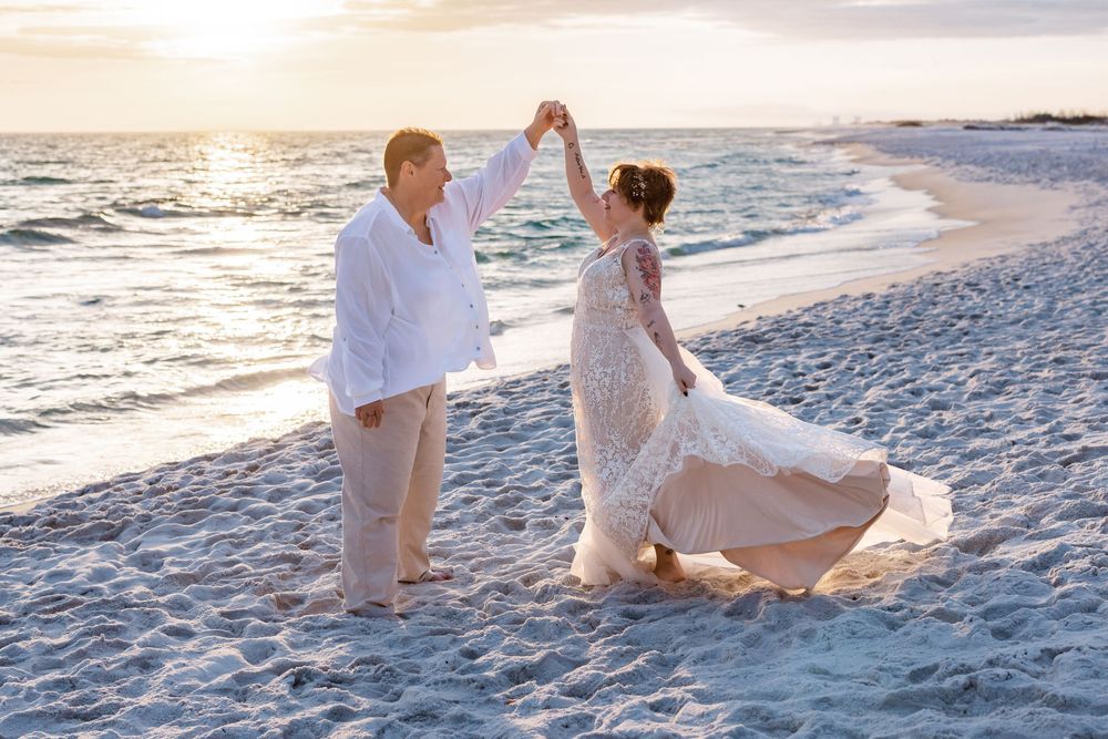A couple dances together on a pristine white sand beach at sunset creating romantic silhouettes against the ocean.