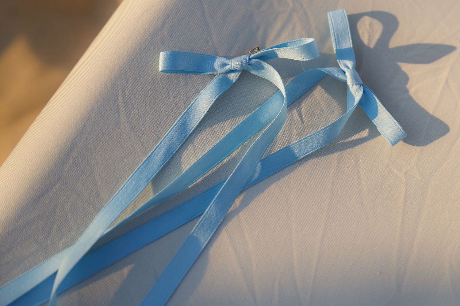 Blue satin ribbon bow being tied in stages against a white background.
