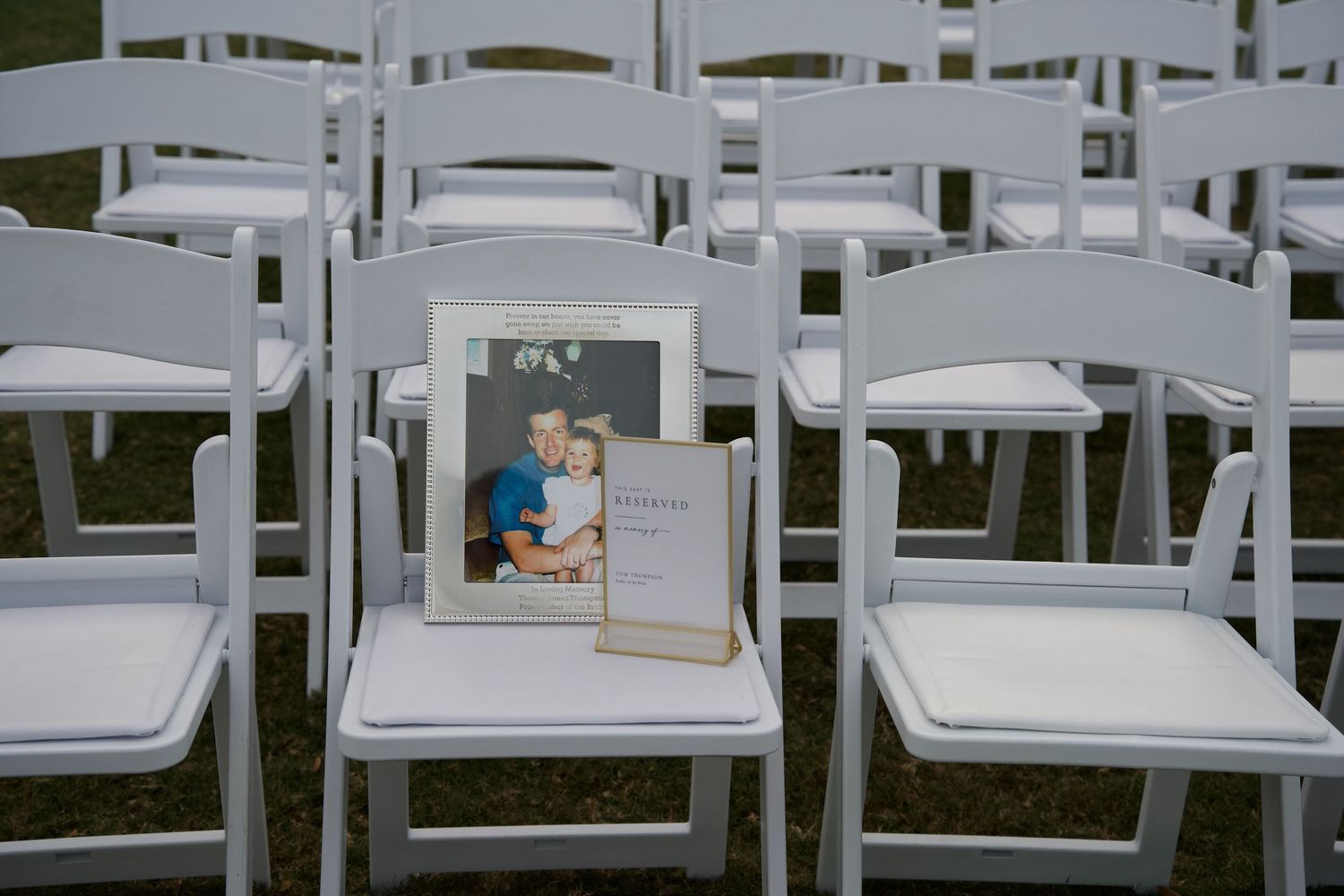 A sequence of white plastic outdoor chairs arranged in rows on grass for an outdoor event or ceremony.