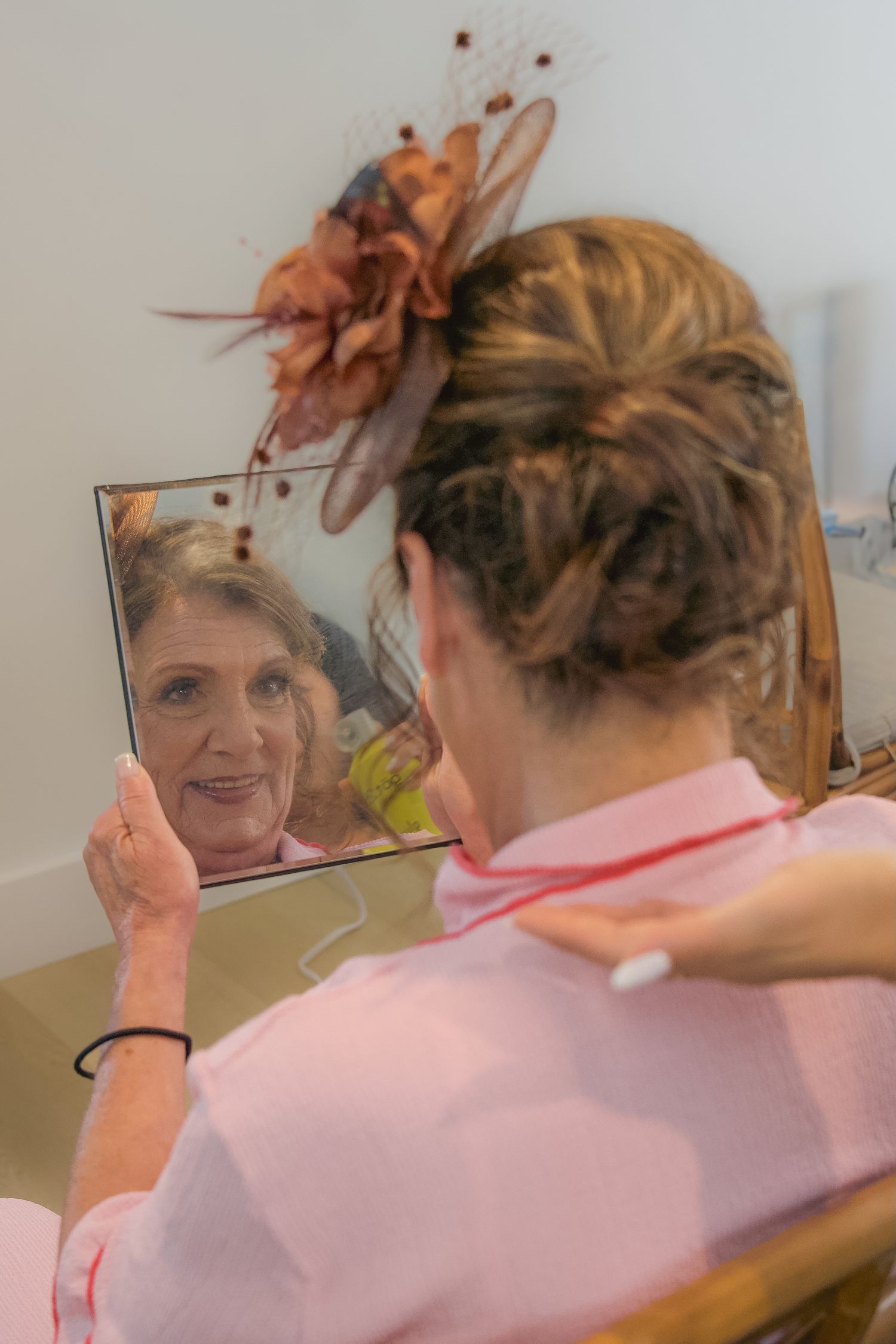 Someone adjusts a peach-colored hair accessory while looking in a mirror, wearing a pink top.