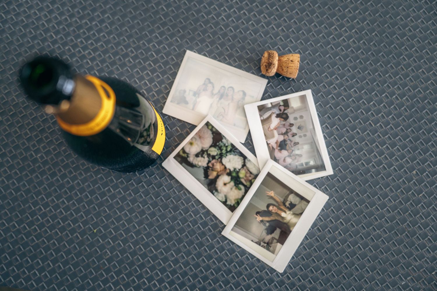 Vintage polaroid photographs scattered on a dark textured surface with a glass bottle in the corner.