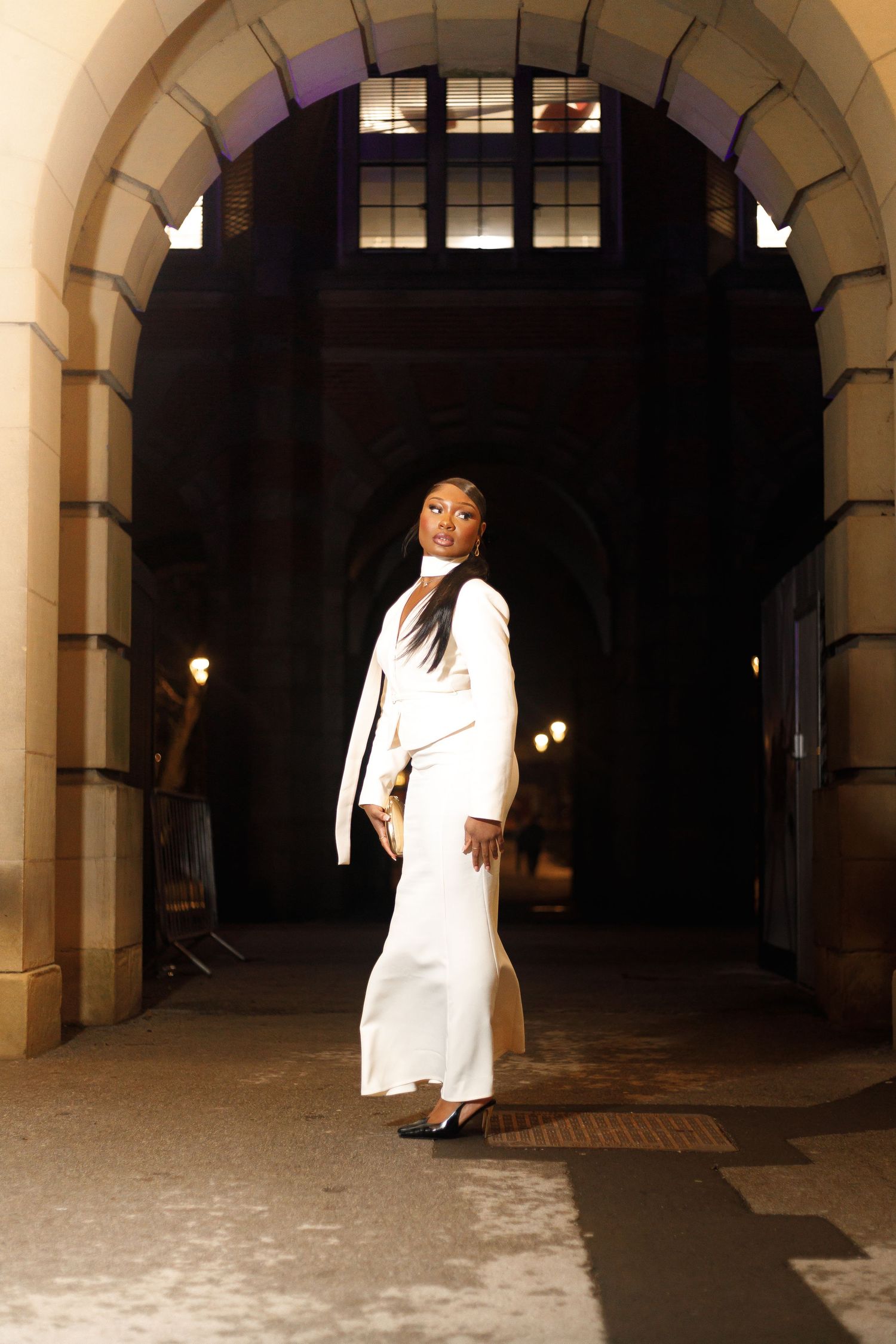A person in white clothing performs dramatic poses in an arched stone hallway at night.