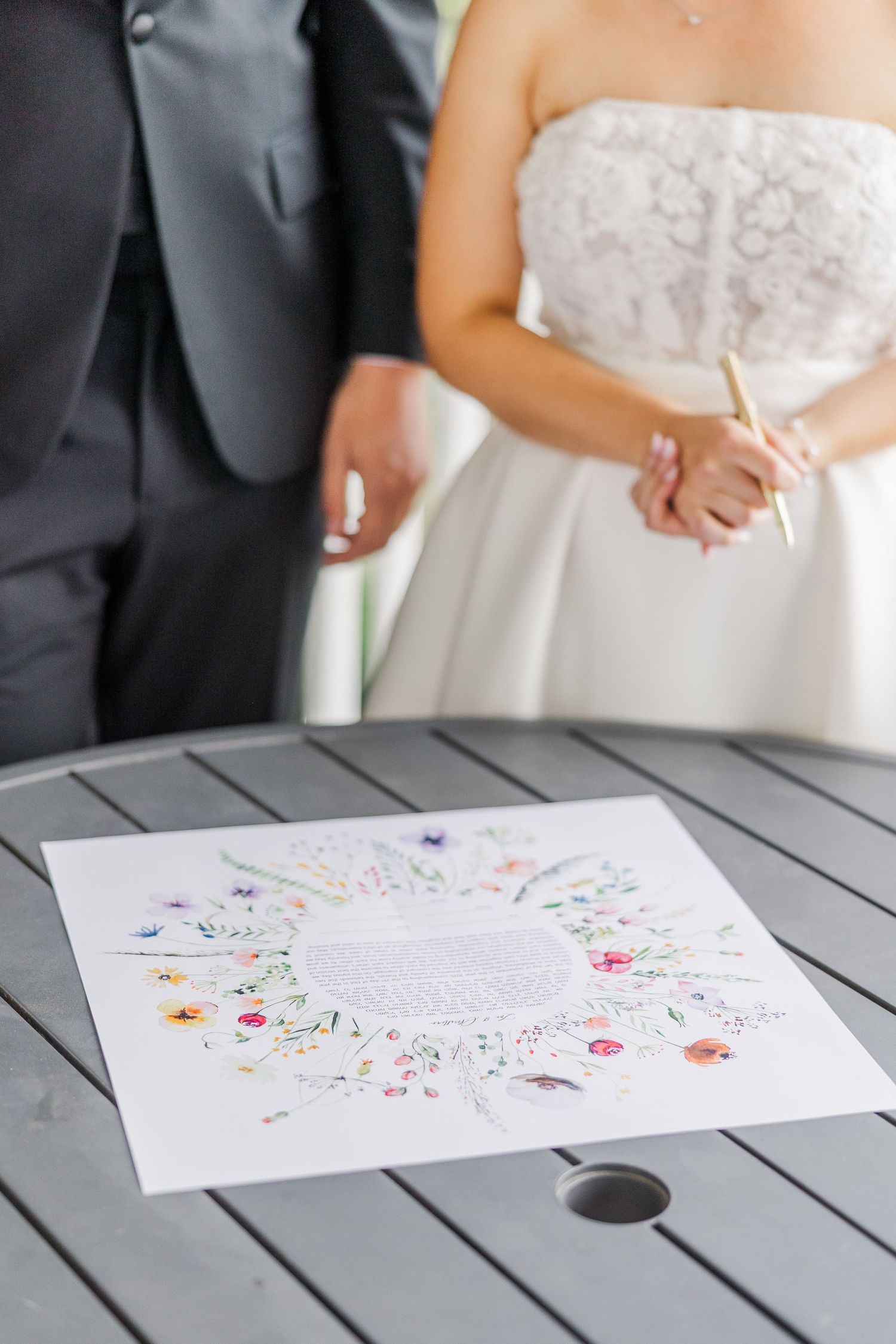 Close-up of a floral decorated document being signed during a wedding ceremony.