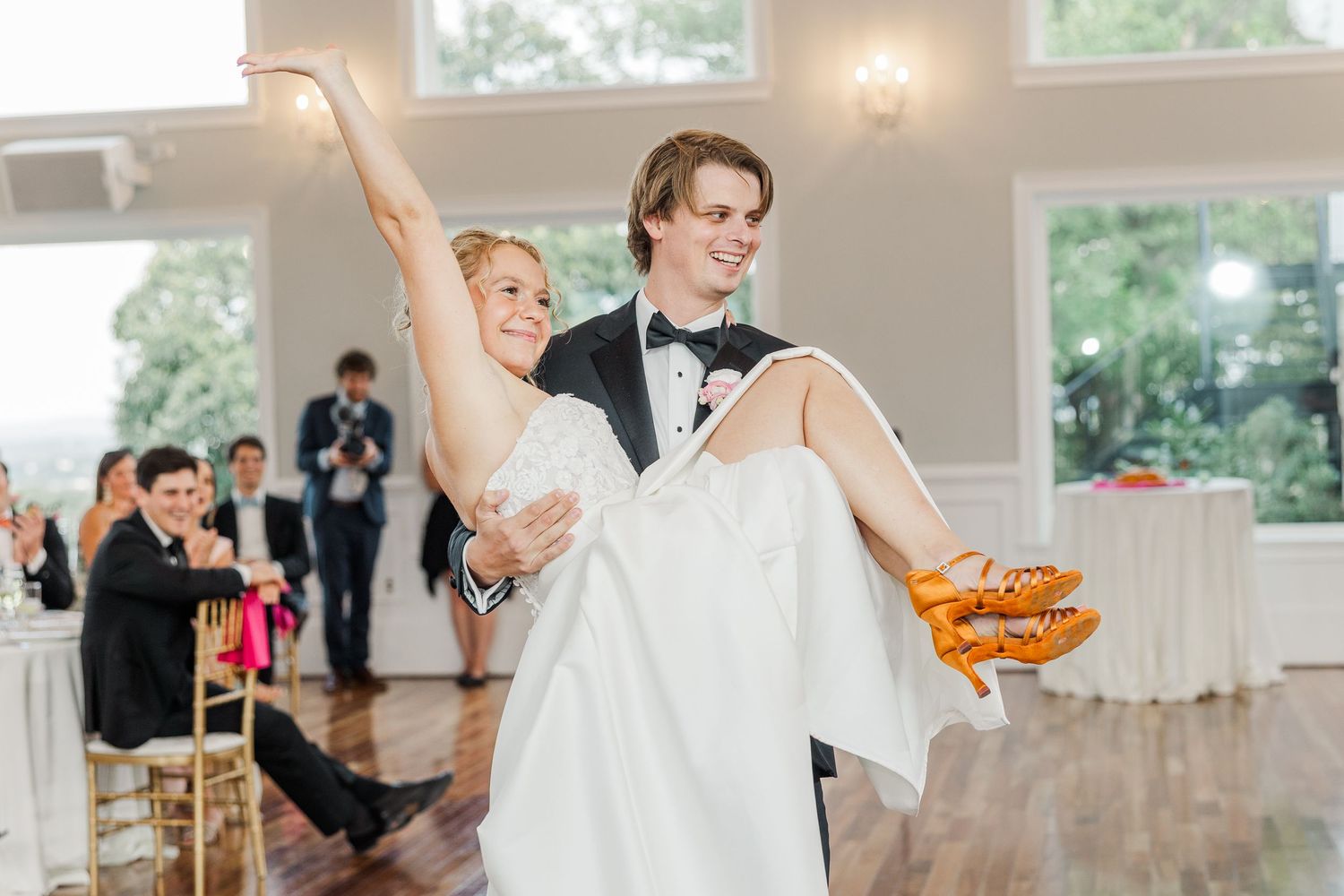 Groom lifts bride during a playful moment at their wedding reception in an elegant white ballroom.