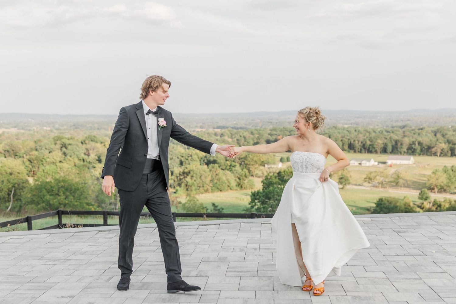 A playful wedding scene on a stone patio overlooking rolling hills.