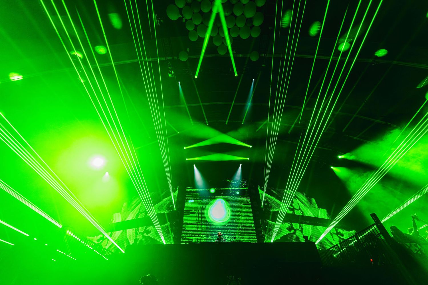 Vibrant green laser beams illuminate a dark concert venue with dramatic lighting effects during a performance.