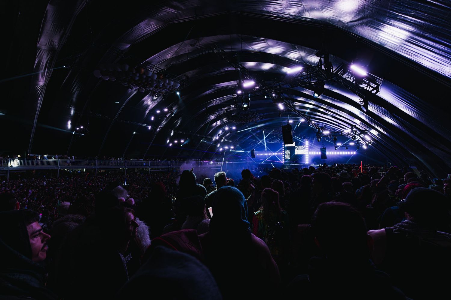 Concert crowd in a dark arched venue with blue stage lighting illuminating a curved ceiling during live performance.