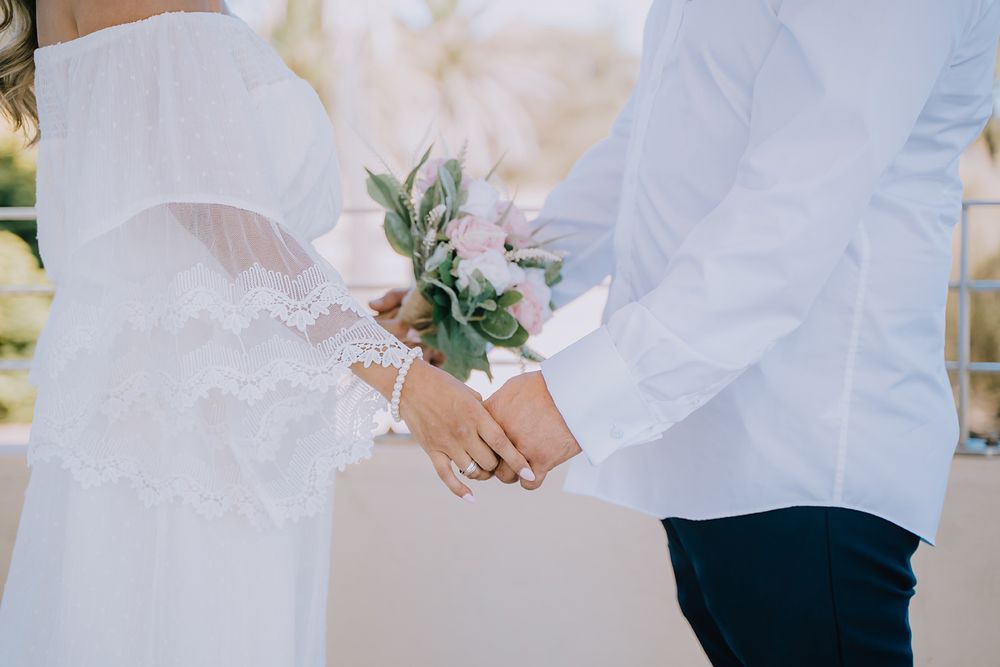 Close-up of couple holding hands during outdoor wedding ceremony with white floral details.