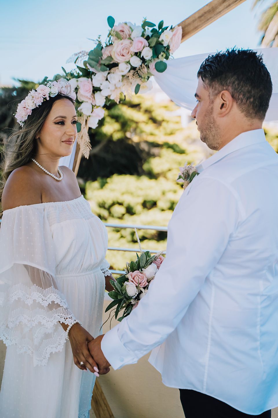 A romantic outdoor wedding scene with a couple standing beneath a white canopy decorated with pink flowers.