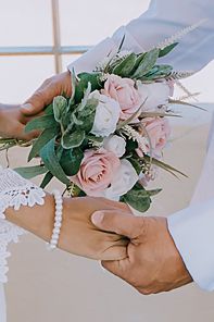Hands holding a delicate pink rose bouquet with eucalyptus leaves and pearl bracelet against light background.