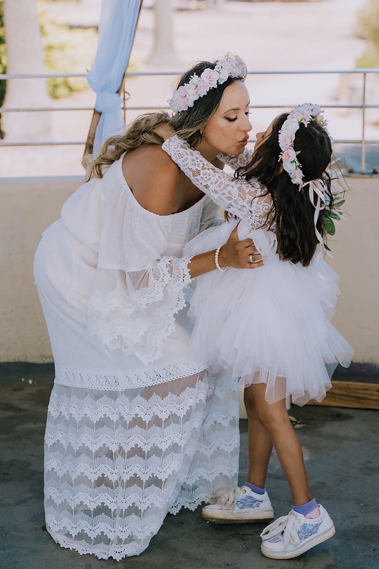 Sweet moment between bride and flower girl wearing matching white dresses and floral crowns.