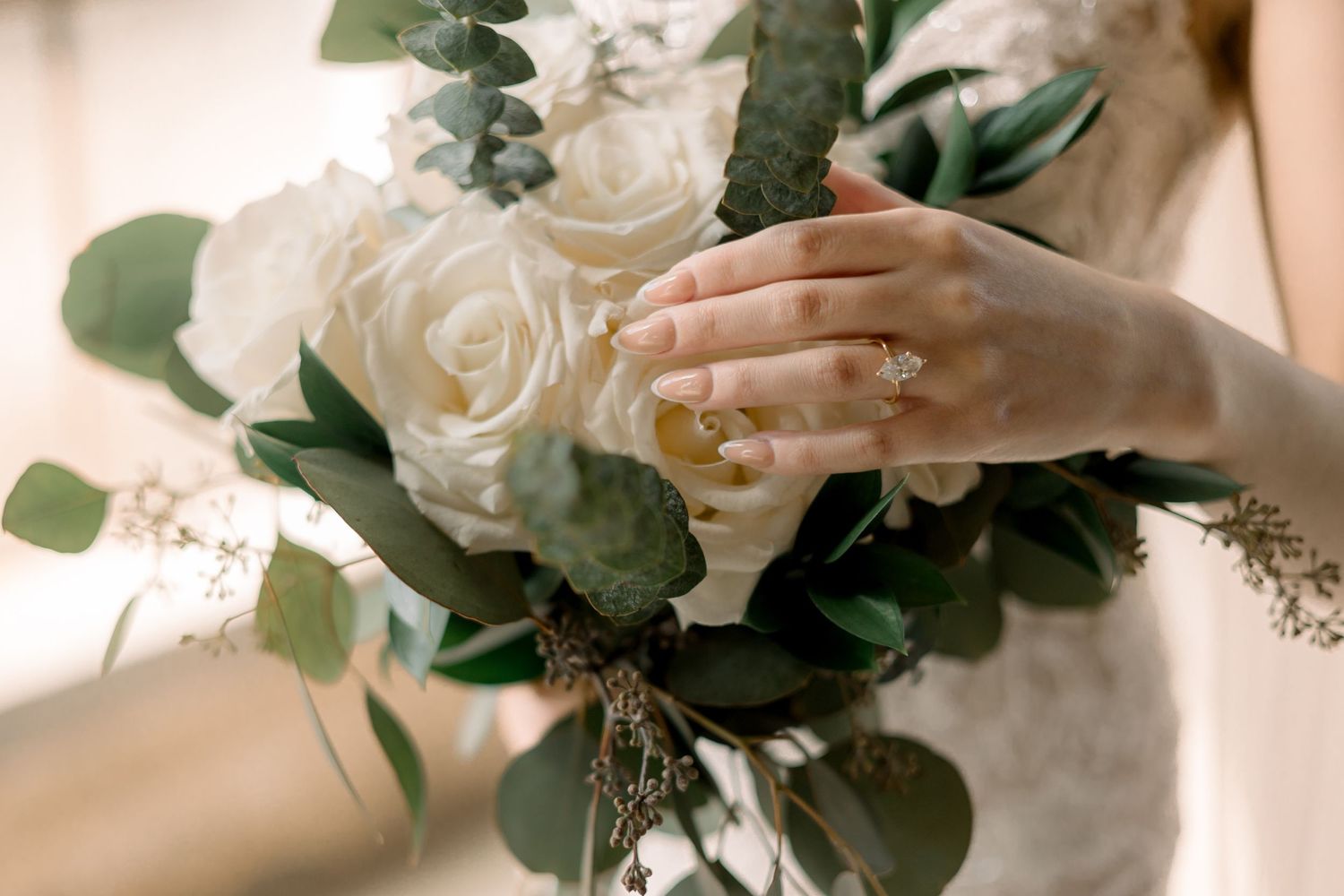 Elegant white rose bouquet with eucalyptus leaves held by hands wearing a wedding ring.