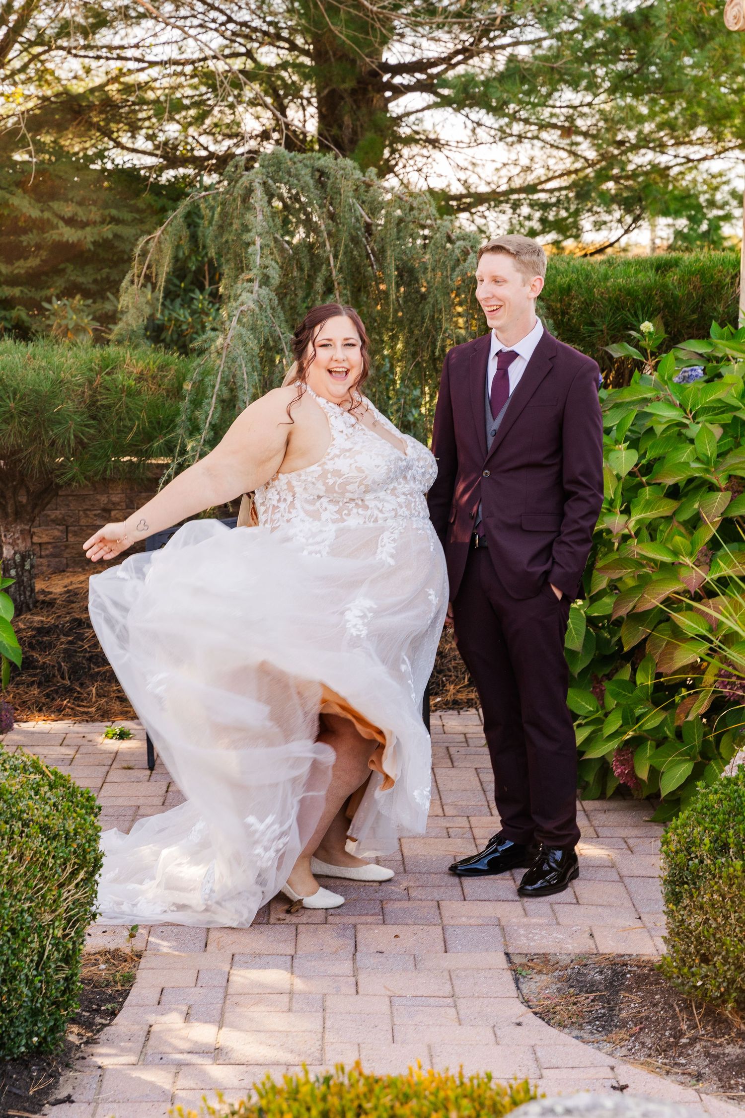Wedding couple shares a playful moment on a garden path beneath a weeping willow tree.