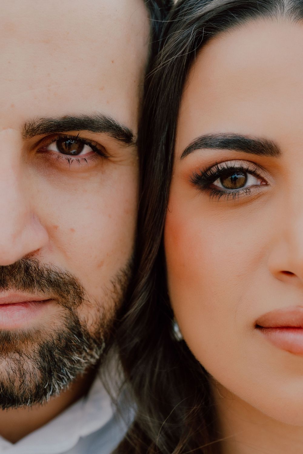 Close-up portrait of a couple with brown eyes, man with beard and woman with elegant makeup, faces side by side.