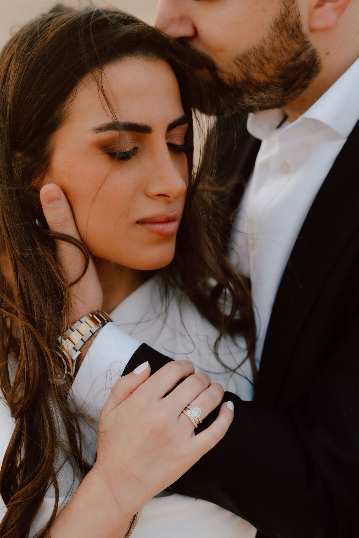 Romantic couple embracing, woman with ring holding man in suit, soft intimate moment with eyes closed.