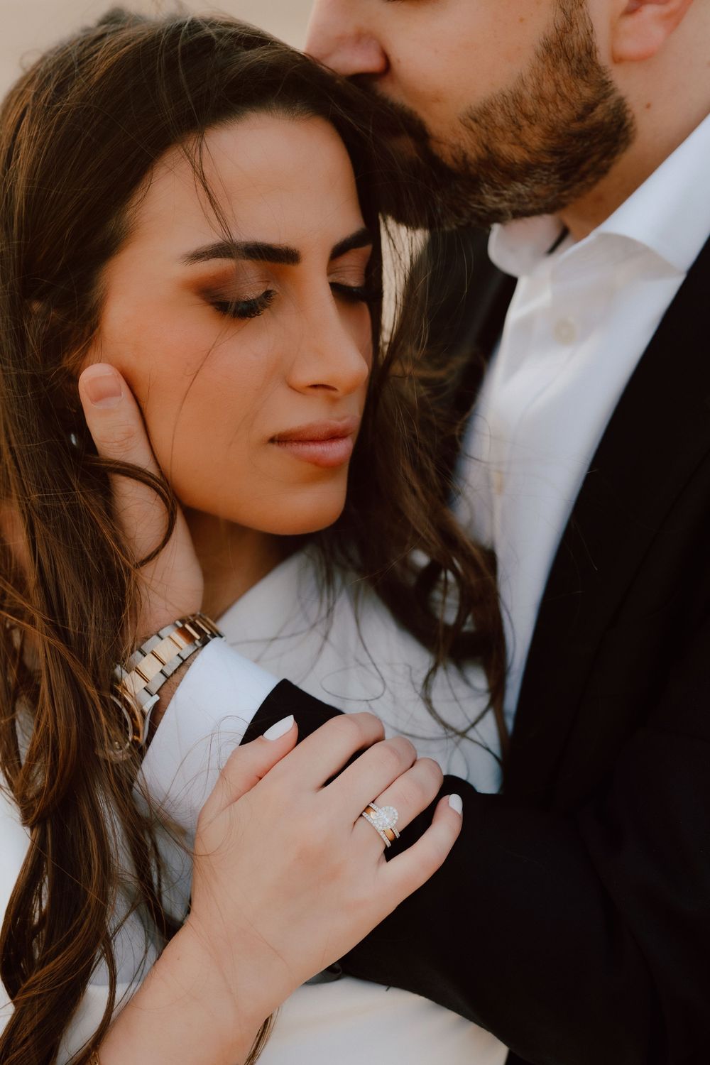 Romantic couple embracing, woman with ring holding man in suit, soft intimate moment with eyes closed.