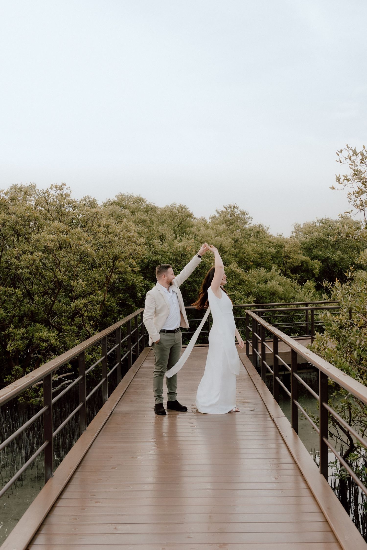 Symmetrical composition of bride and groom walking on long wooden walkway during wedding shoot