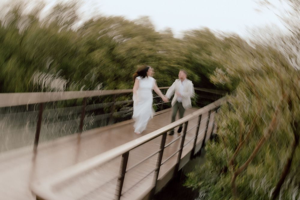 Creative motion blur wedding photo of couple walking across wooden bridge