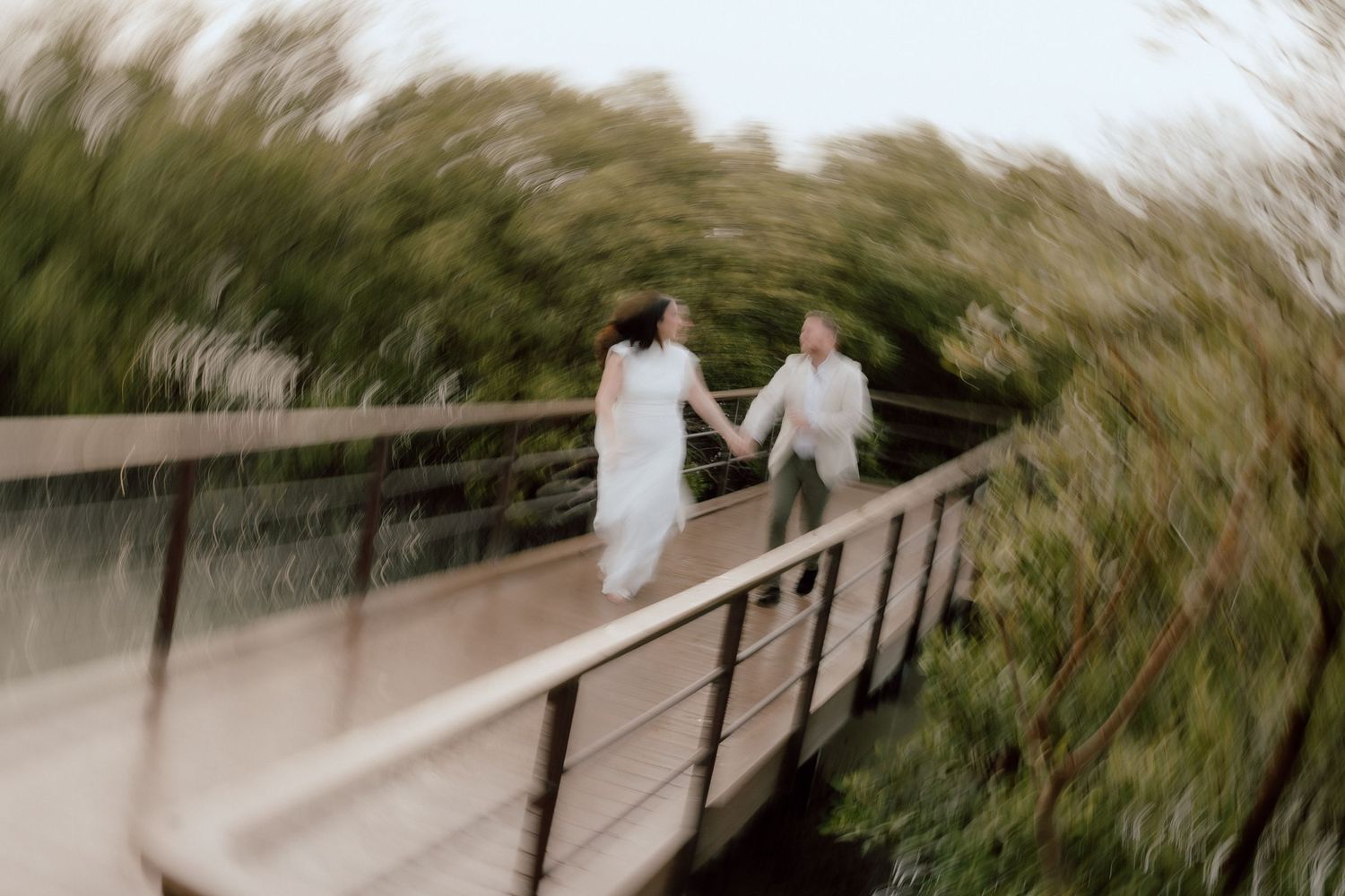 Creative motion blur wedding photo of couple walking across wooden bridge