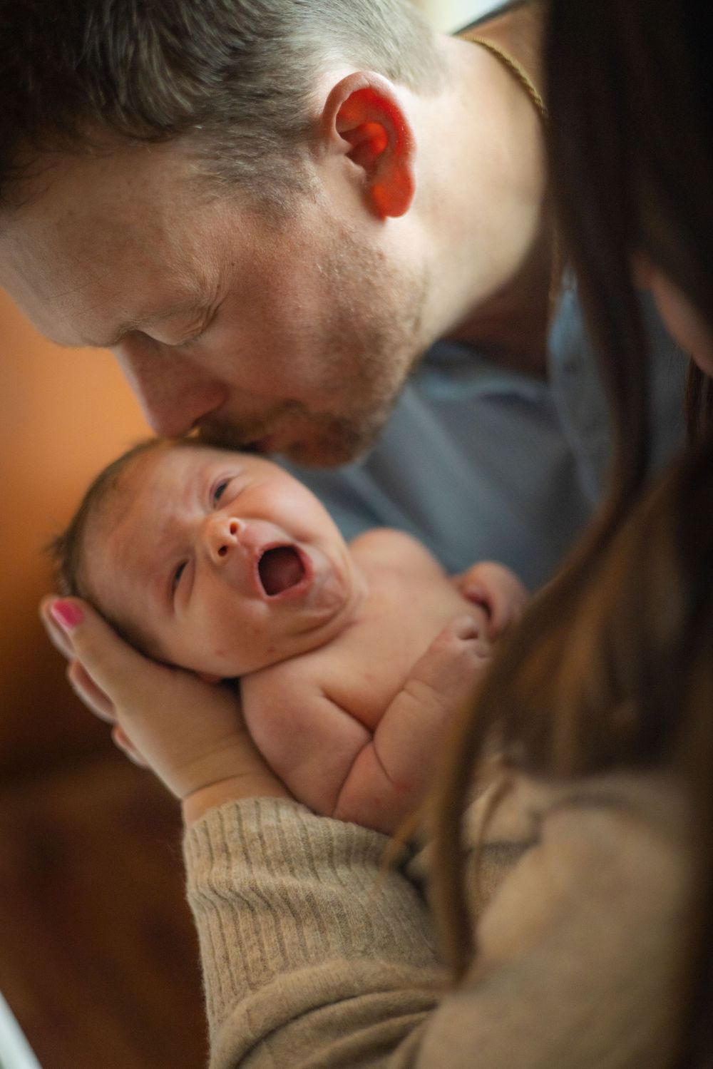 A yawning newborn baby is held close by an adult in a beige sweater.